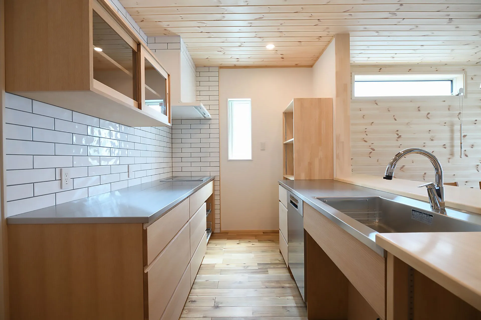 明るい木製システムキッチン。白タイルと無垢材の天井。ナチュラルインテリア。