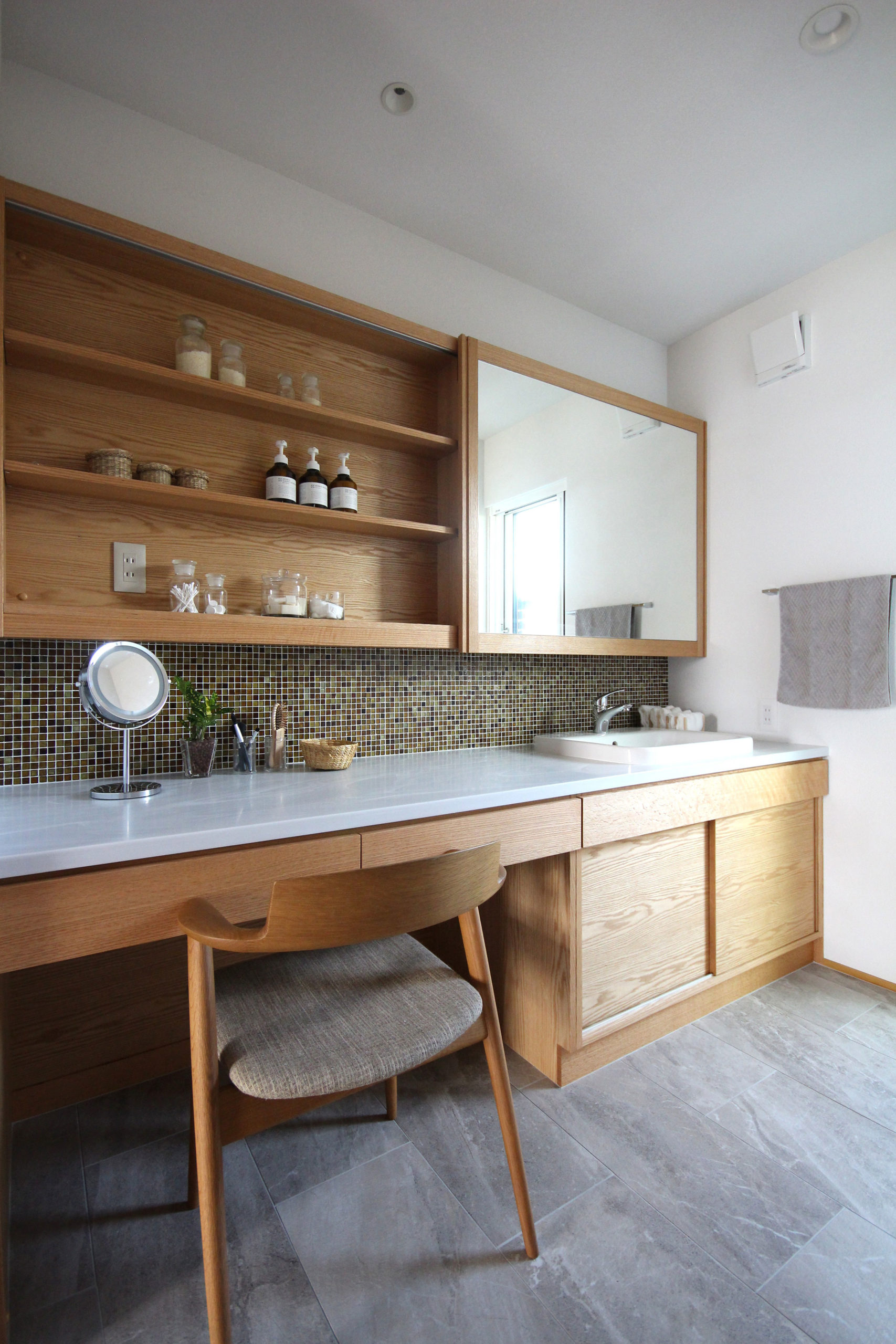 モザイクタイル壁と木製収納棚のある、ドレッサー機能を備えたナチュラルな洗面スペース