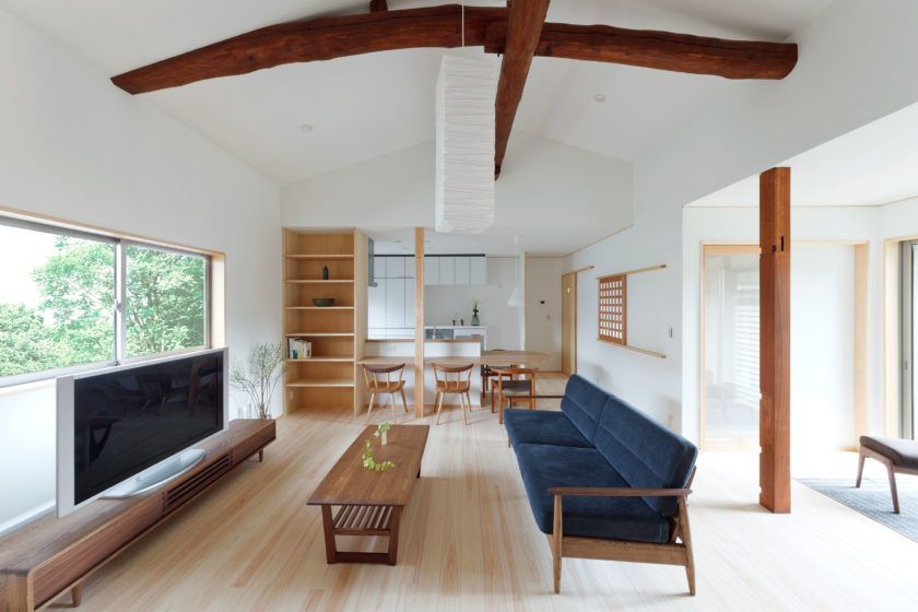 木製家具とネイビーのソファが配置された、勾配天井と大きな窓のあるナチュラルなリビングダイニング空間