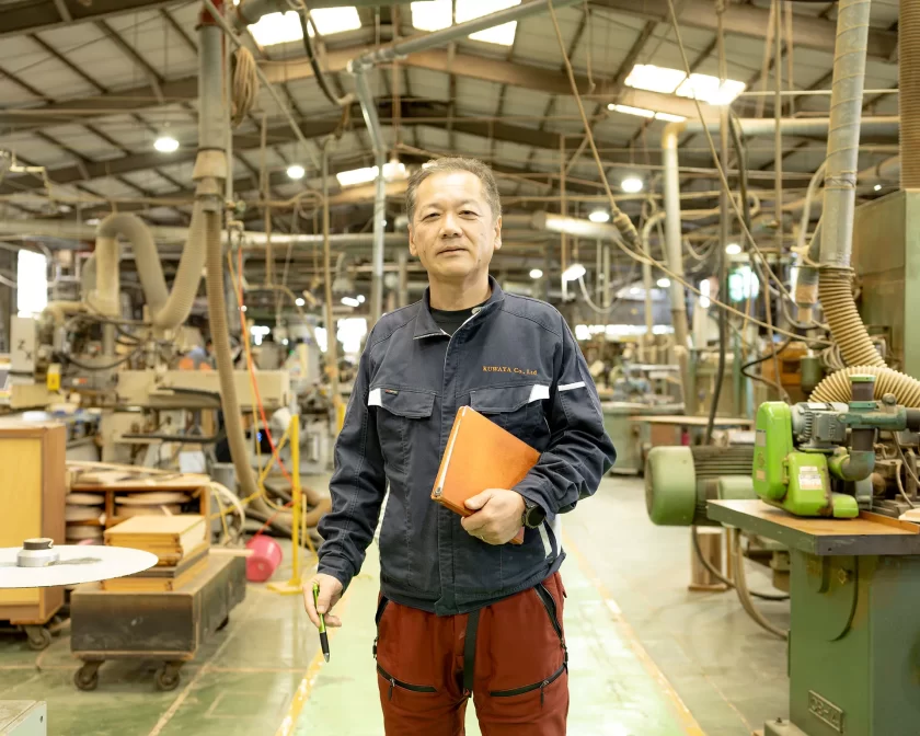 木工機械が並ぶ久和屋の自社工場内に立つ澤口工場長の全身近影